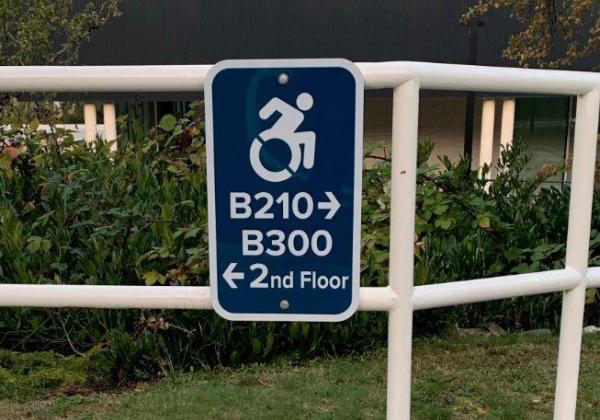 A sign with a wheelchair symbol posted on a railing outside