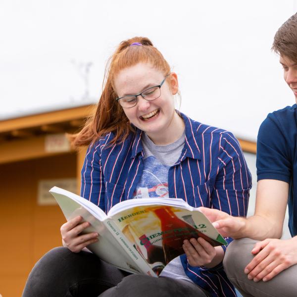 Two teens reading a textbook together