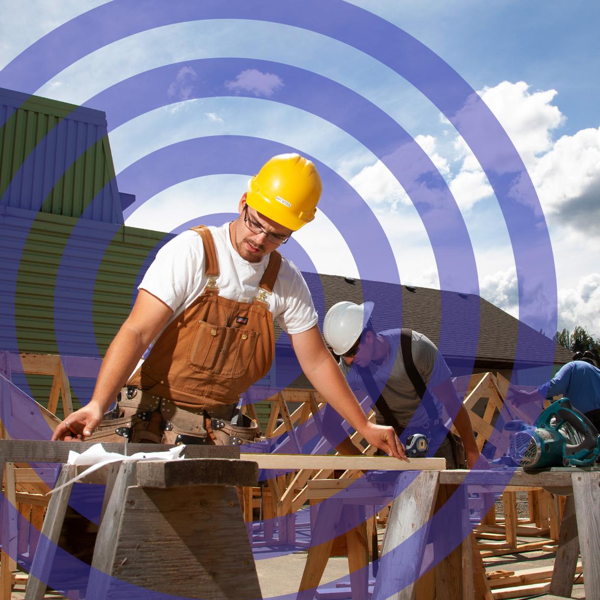 A man in a hardhat working at a sawhorse under a blue sky. 