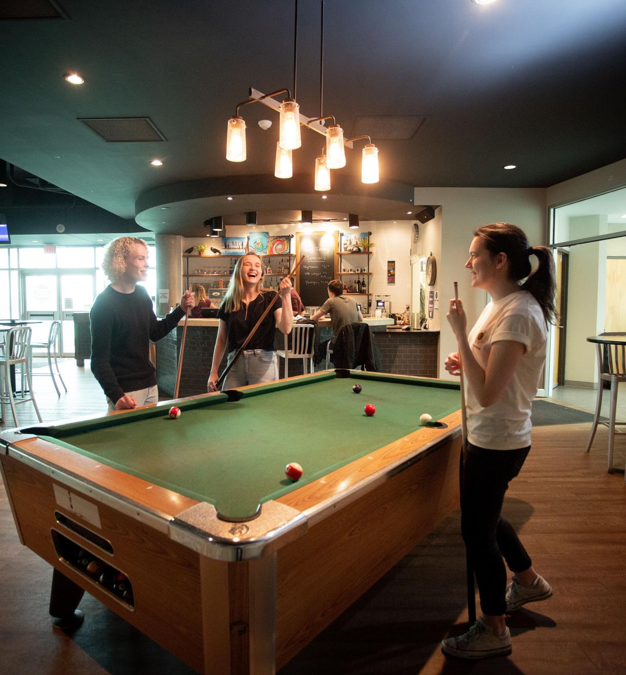 Three students play pool at the campus pub