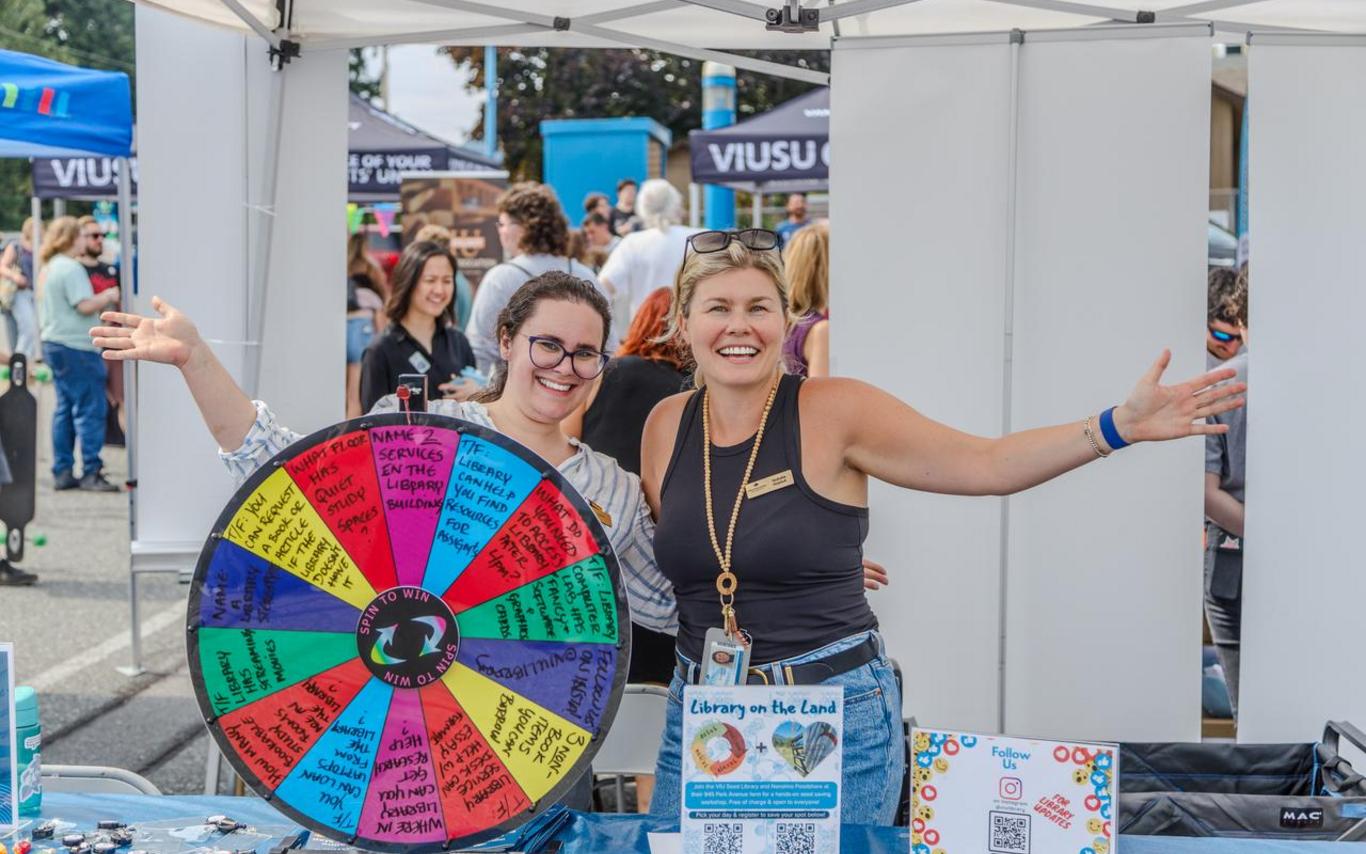 two women spread their arms wide behind a game wheel