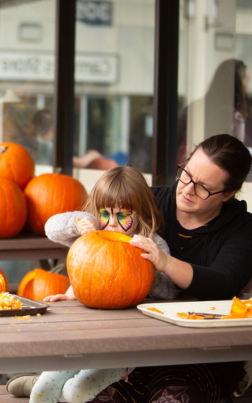 Child carving a pumpkin with an adult.